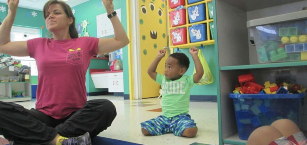 Woman and small boy inside a classroom with hands above their head