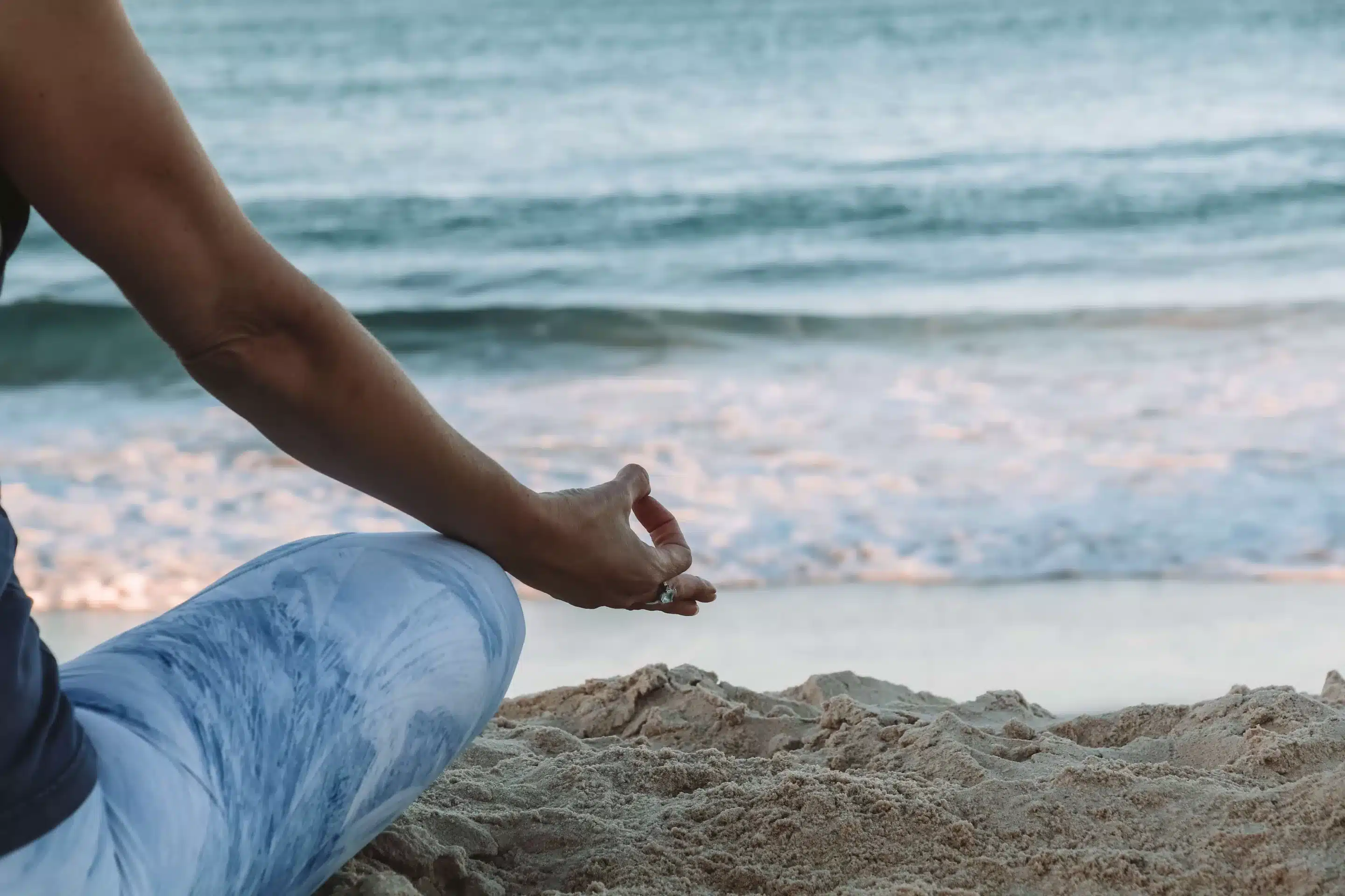 A woman meditating at the beach with her hand in a mudra position